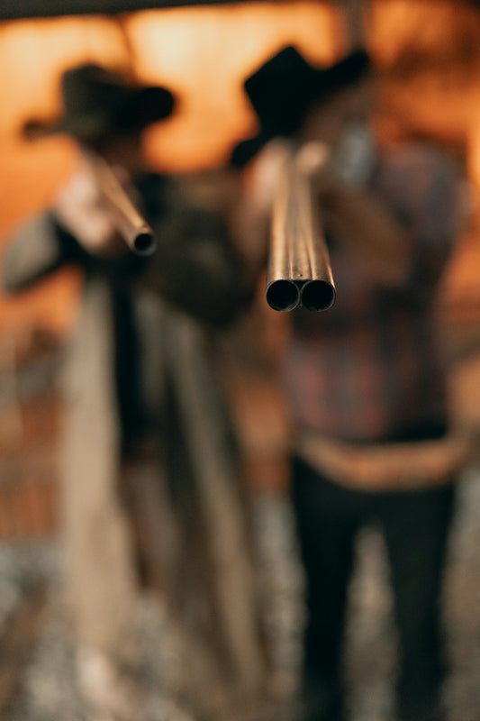 Two cowboys aim shotguns with focus on barrels